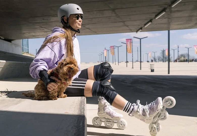 A girl in roller skates and a helmet sits next to her dog